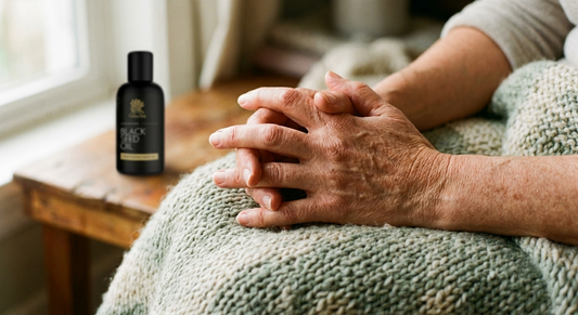 Relaxed mature hands resting comfortably on a soft sage blanket in warm light with a black seed oil bottle out of focus behind, evoking joint comfort