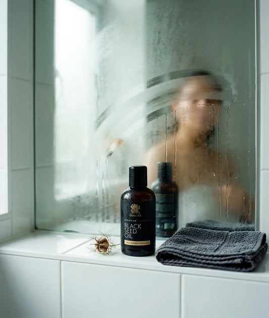 Amber bottle of organic black seed oil on a bathroom shelf before a steamed mirror