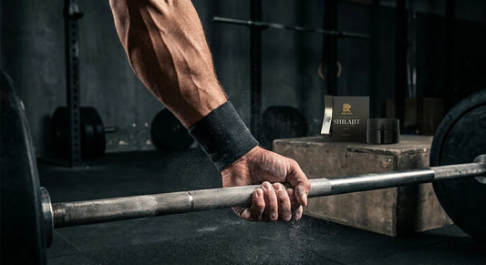 Low-angle shot of a muscular forearm gripping a chalk-dusted steel barbell with a pot of shilajit resin on a ledge behind, linking supplement to strength